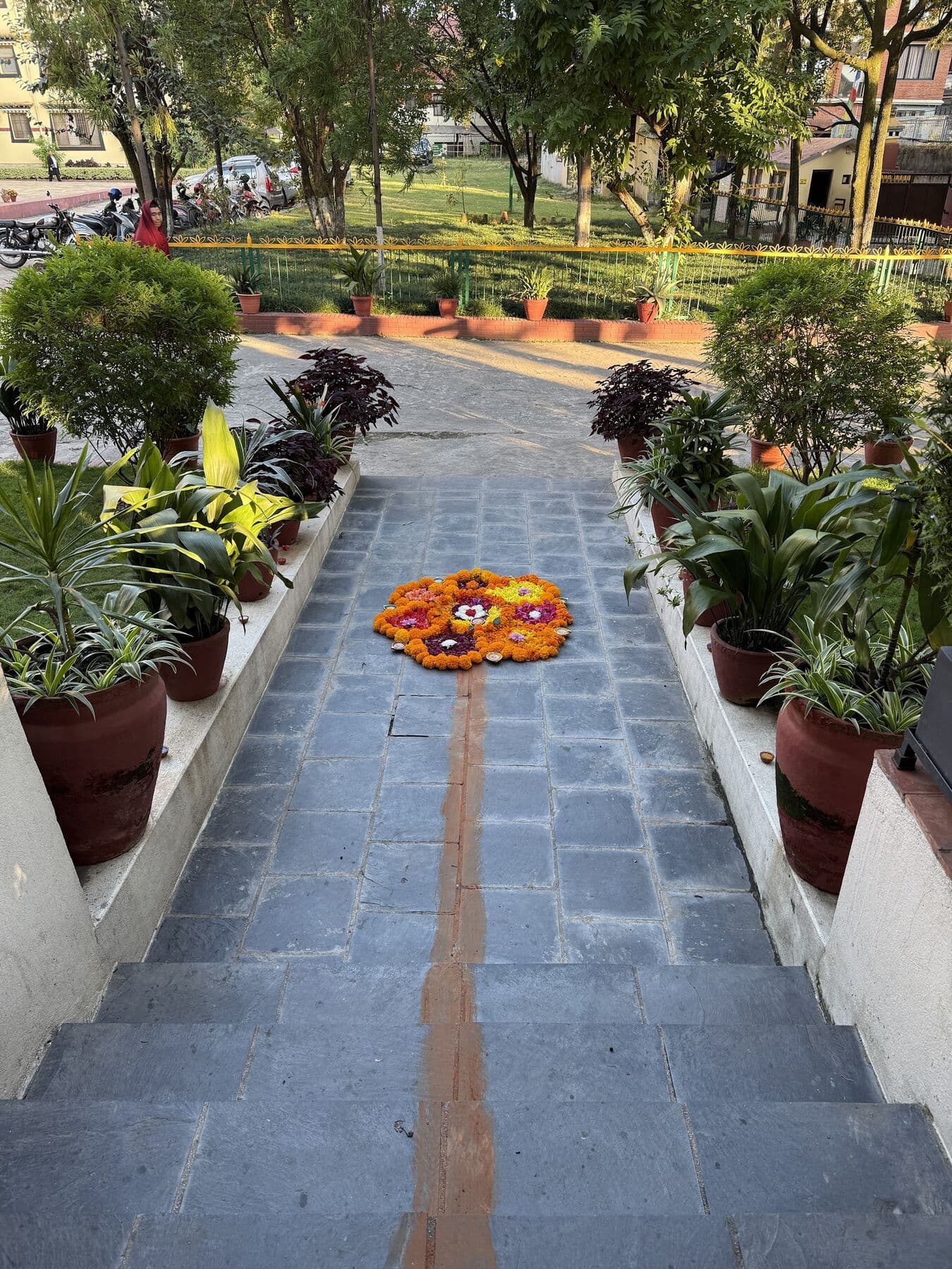 A stone path between potted plants leading to the monastery lawn