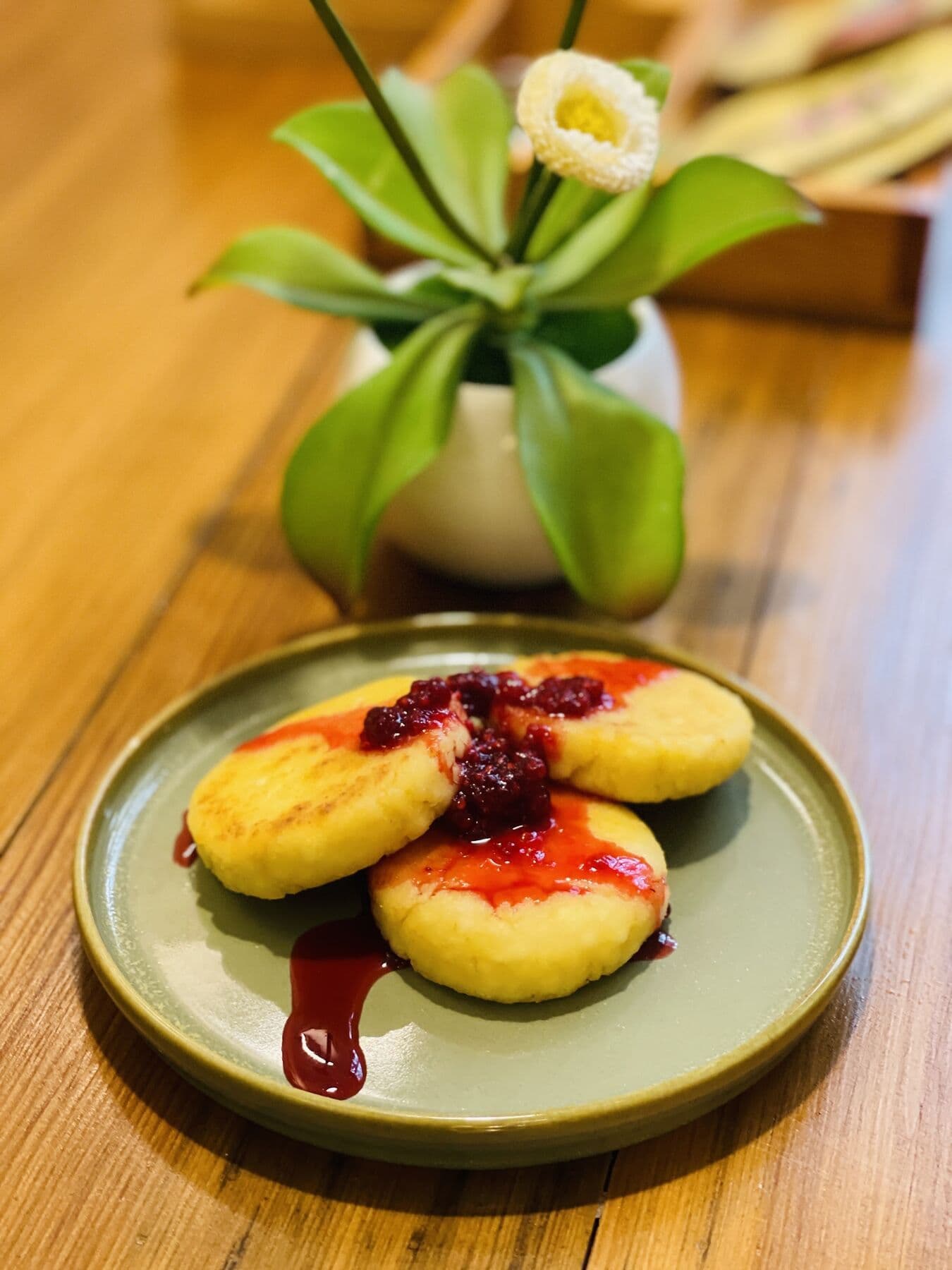Small pancakes with berry sauce beside a vase of flowers